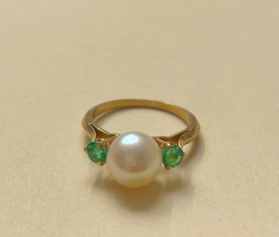 un gros plan d'une bague ornée d'une perle et d'une émeraude posée sur une table
