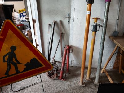 a yellow and red road sign sitting next to a pile of tools