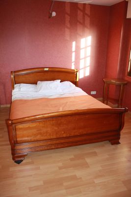 a wooden bed in a room with a red wall