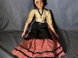 La poupée porte une robe rouge et blanche et des chaussures noires.