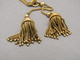 two gold tassels hanging from a chain on a gray surface