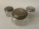 three glass jars with silver lids sitting on a table