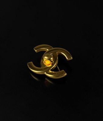 a close up of a gold chanel broocher on a black surface