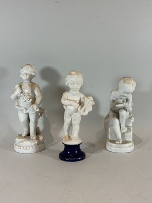three figurines of children sitting on pedestals on a white surface