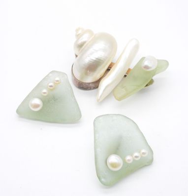 trois morceaux de verre de mer, accompagnés de perles et d'un coquillage, posés sur un fond blanc