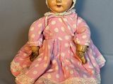 Une vieille poupée vêtue d'une robe rose et d'un bonnet est assise sur une surface grise