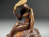 bronze sculpture of a woman sitting on a rock with a hat on her head
