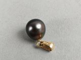 a black pearl with a gold clasp on a gray surface