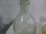 une bouteille en verre vert et un bol en verre vert sur un tissu blanc