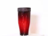 un verre rouge avec un couvercle noir posé sur une étagère blanche