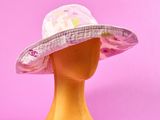 un chapeau rose et blanc posé sur une tête de mannequin, sur fond rose