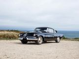 an old black car parked on a gravel road near the ocean