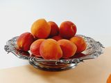 a bowl of apricots and an orange on a table