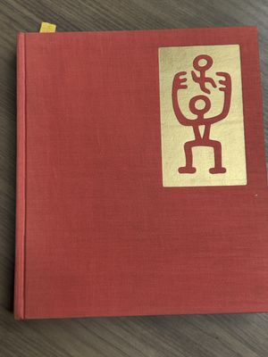 an old red book with a gold sticker on it sitting on a wooden table