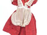 une poupée vêtue d'une robe rouge et d'un bonnet, assise sur une boîte
