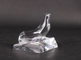a clear glass sculpture of a bird on a rock on a black surface