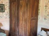 a wooden armoire in the corner of a room with floral wallpaper