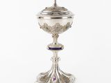une coupe en argent surmontée d'une croix, posée sur un fond blanc