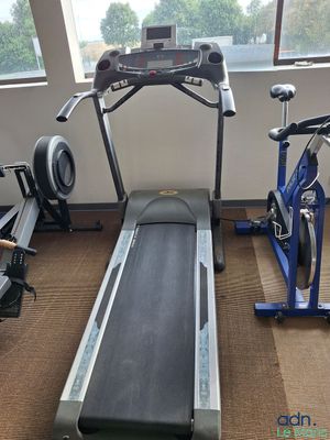 un tapis de course dans une salle de sport, avec une fenêtre en arrière-plan