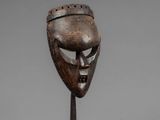 a wooden mask on a metal stand with a gray background