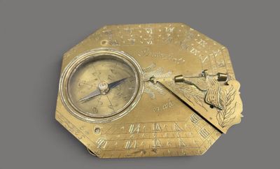 an antique brass compass on a gray surface with a clock