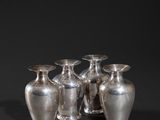 four silver vases sitting on top of a black surface