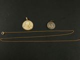 deux colliers en or et en argent et une pièce de monnaie posés sur une surface noire