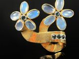 an image of a gold and blue flower broochle on a black surface