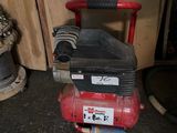 a red air compressor sitting on the floor next to a fire hydrant