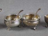 five silver cups and spoons are lined up on a table