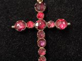 un pendentif en forme de croix en pierre rose posé sur un fond de velours noir