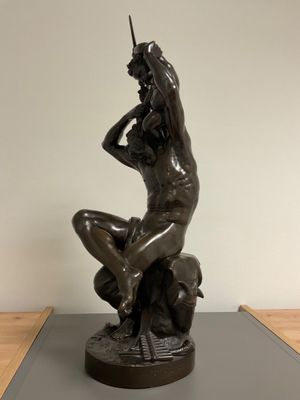 bronze statue of a woman sitting on a rock with her hands on her head