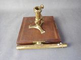 un microscope ancien plaqué laiton, posé sur un socle en bois, sur une surface grise