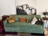 a green couch in a living room with a painting on the wall