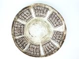 une assiette en argent posée sur un fond blanc et ornée d'un motif