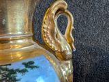 a gold vase with a painting on it sitting on a red cloth