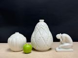 three white vases sitting on a table next to a green apple