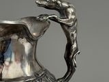 an antique silver pitcher with a dog on it ' s handle