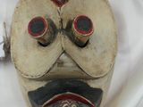 un masque en bois posé sur un drap blanc, avec une brosse à dents