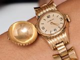 a gold watch on a woman ' s wrist with a gold ball on it