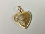 a close up of a gold heart shaped pendant on a white surface