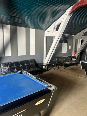 une table de billard au milieu d'une pièce où se trouvent des chaises et une échelle