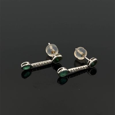 une paire de boucles d'oreilles en argent et émeraude posées sur un fond noir