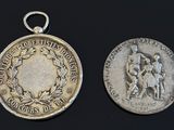 two silver medals with a man and woman on them on a black surface