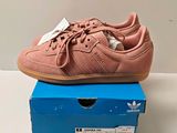 des baskets Adidas roses posées sur une boîte bleue, sur une surface blanche