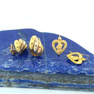 a close up of three pairs of gold earrings on a blue stone
