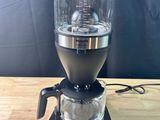 an image of a coffee maker on a wooden table with a black background