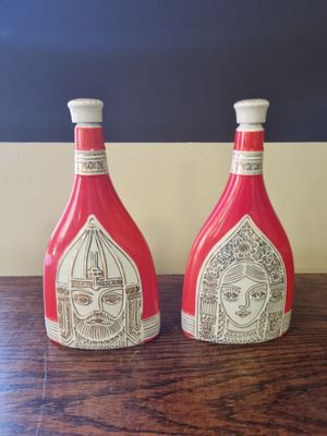 pair of red and white bottles with faces on them sitting on a wooden table