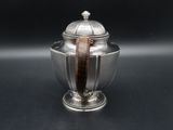 an antique silver teapot with a wooden handle on a black surface