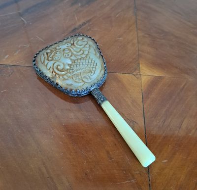 un petit miroir posé sur une table en bois, muni d'une poignée en bois